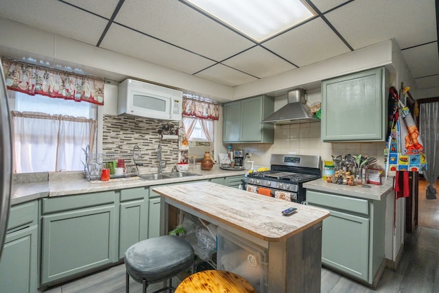 kitchen featuring wall chimney exhaust hood, a drop ceiling, light hardwood / wood-style floors, gas range, and sink