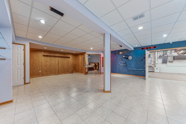 basement with light tile patterned flooring, a drop ceiling, and wooden walls