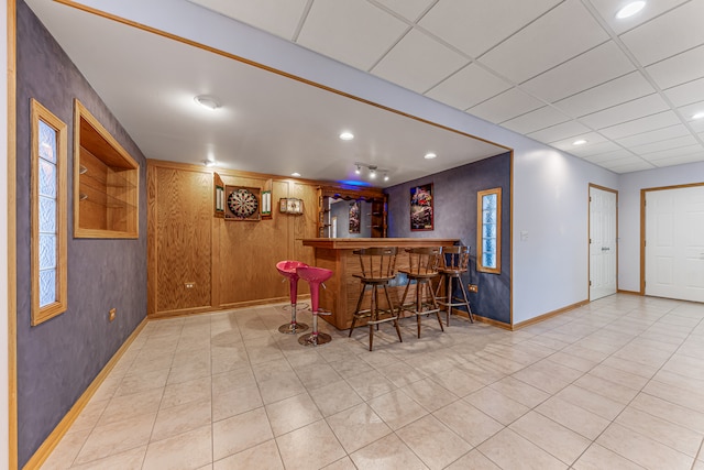 bar featuring wood walls, a paneled ceiling, and light tile patterned floors