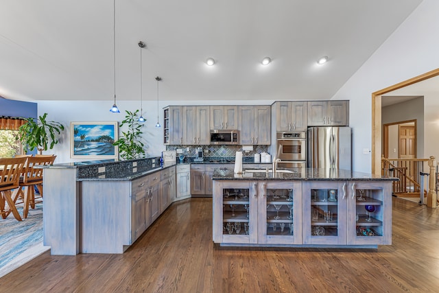 kitchen featuring lofted ceiling, dark wood-type flooring, hanging light fixtures, stainless steel appliances, and dark stone countertops