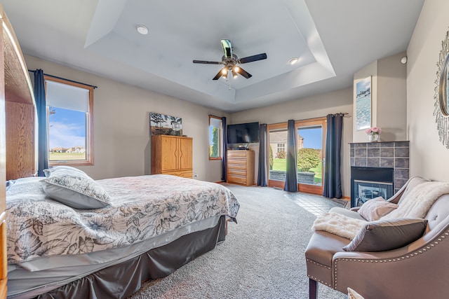 carpeted bedroom with ceiling fan, a raised ceiling, access to outside, and a tile fireplace