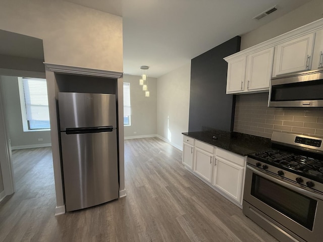 kitchen featuring light wood-type flooring, tasteful backsplash, stainless steel appliances, dark stone countertops, and white cabinets