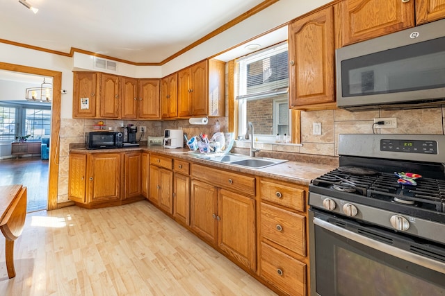 kitchen with light hardwood / wood-style floors, crown molding, sink, backsplash, and appliances with stainless steel finishes