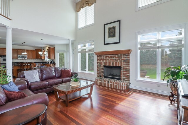 living room featuring decorative columns, a fireplace, a towering ceiling, and hardwood / wood-style floors