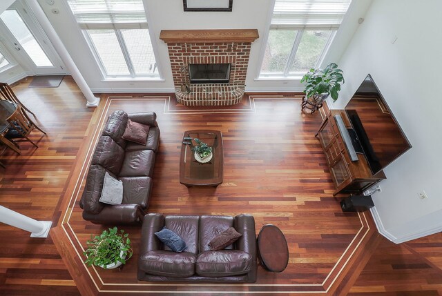 living room with ornate columns, a brick fireplace, and wood-type flooring