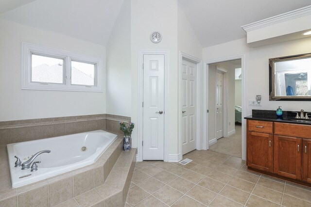 bathroom with a relaxing tiled tub, vanity, lofted ceiling, and tile patterned flooring