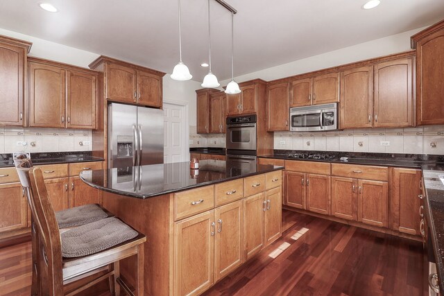 kitchen featuring appliances with stainless steel finishes, hanging light fixtures, dark hardwood / wood-style floors, and backsplash