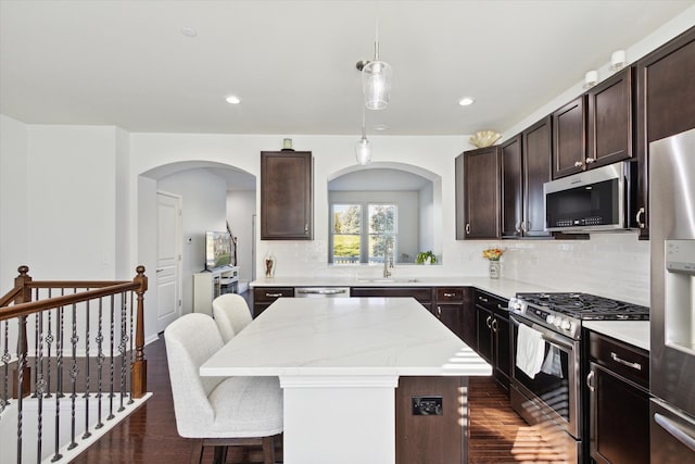 kitchen with a kitchen island, dark wood-type flooring, stainless steel appliances, sink, and pendant lighting