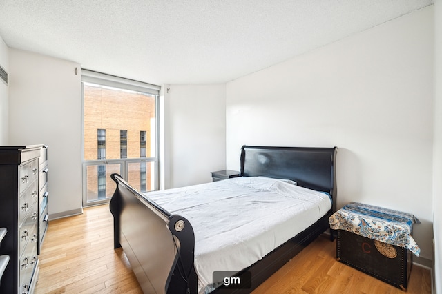 bedroom featuring floor to ceiling windows, light wood-type flooring, and a textured ceiling