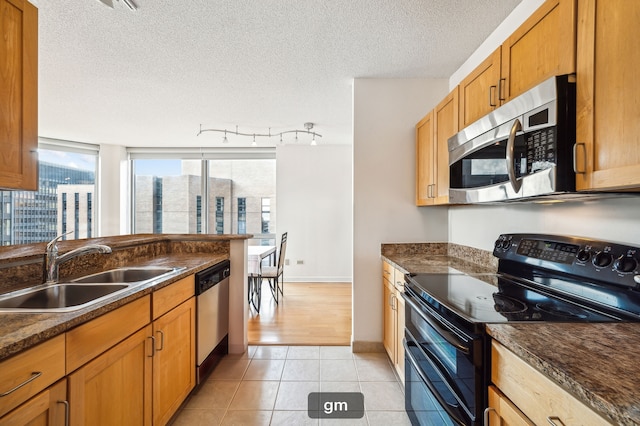 kitchen featuring sink, light tile patterned floors, a textured ceiling, stainless steel appliances, and dark stone countertops