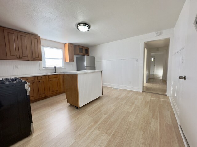 kitchen with light wood-style floors, freestanding refrigerator, black range with gas stovetop, a kitchen island, and a sink
