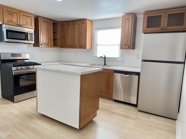 kitchen featuring a sink, light countertops, light wood-type flooring, appliances with stainless steel finishes, and brown cabinetry