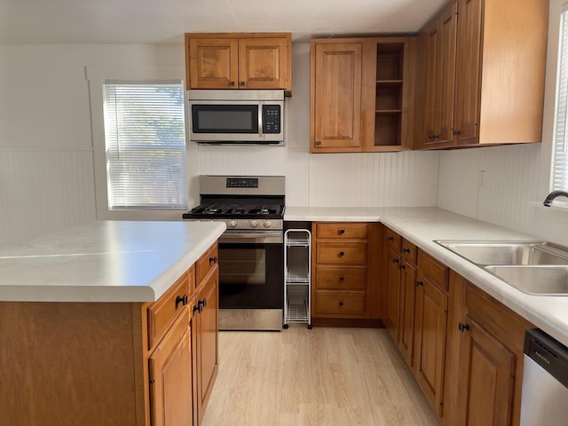 kitchen with a sink, light countertops, brown cabinetry, stainless steel appliances, and light wood-style flooring