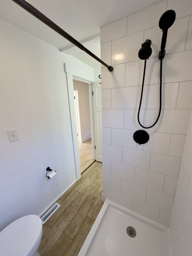 bathroom featuring a tile shower, hardwood / wood-style flooring, and toilet