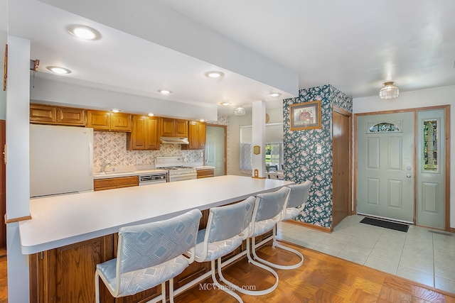 kitchen featuring white appliances, sink, a kitchen bar, light tile patterned floors, and backsplash