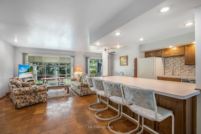 kitchen with ceiling fan, white fridge, dark parquet flooring, a kitchen bar, and backsplash