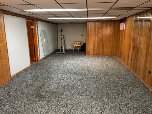 basement with a drop ceiling, wooden walls, and carpet