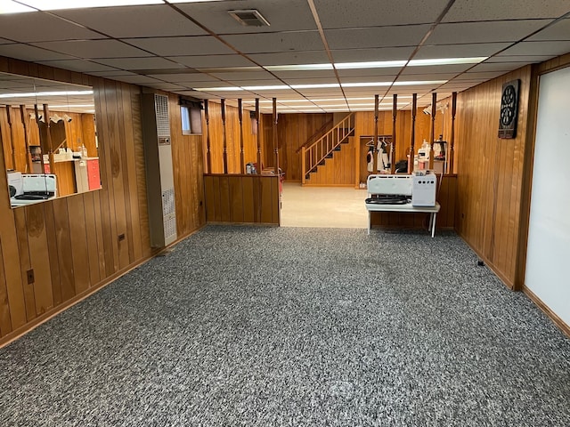 basement with wood walls, carpet floors, and a paneled ceiling