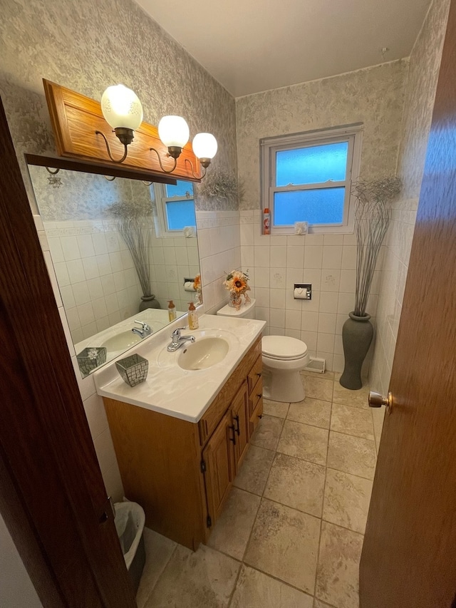 bathroom with a healthy amount of sunlight, vanity, tile walls, and toilet