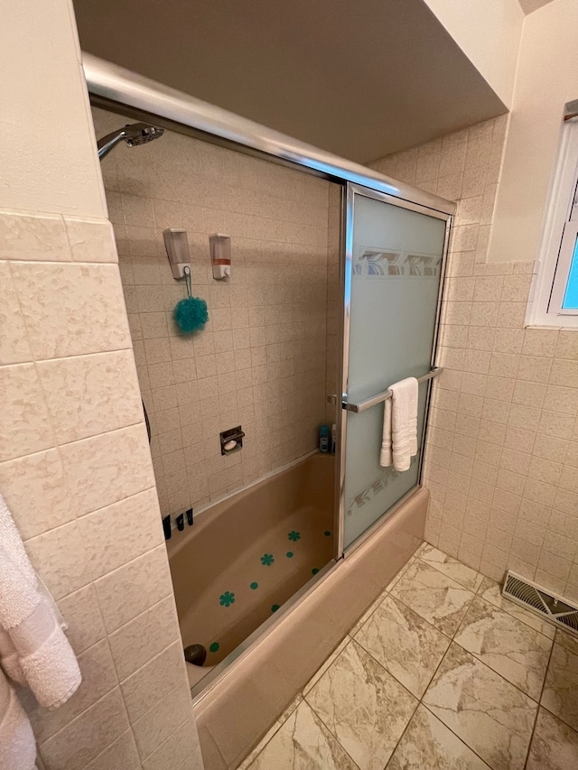 bathroom featuring shower / bath combination with glass door and tile walls