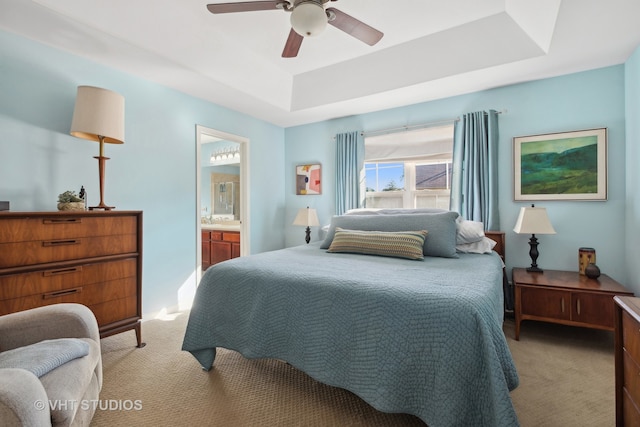 bedroom featuring ensuite bath, a tray ceiling, light colored carpet, and ceiling fan