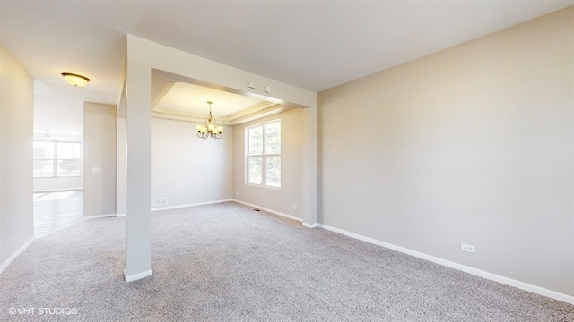 carpeted spare room featuring a tray ceiling and an inviting chandelier