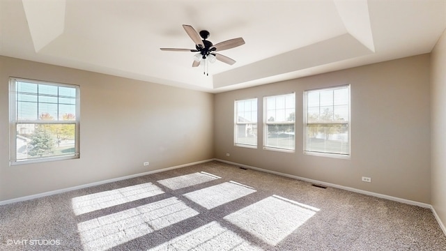 carpeted spare room with ceiling fan, a tray ceiling, and a healthy amount of sunlight