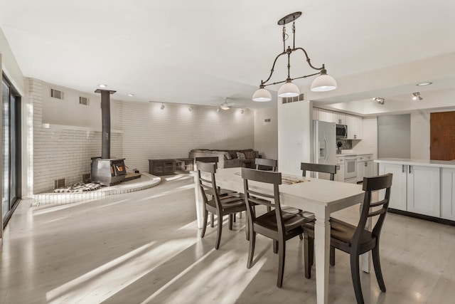 dining area with light hardwood / wood-style flooring, a wood stove, ceiling fan, and brick wall