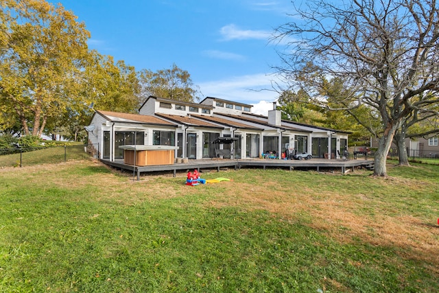 rear view of property featuring a yard, a wooden deck, and a hot tub