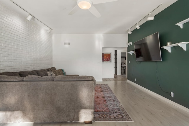 living room with ceiling fan, rail lighting, brick wall, and hardwood / wood-style flooring