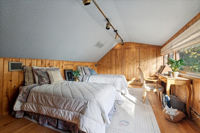 bedroom featuring track lighting, a textured ceiling, hardwood / wood-style flooring, vaulted ceiling, and wooden walls