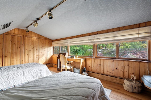 bedroom featuring vaulted ceiling, light wood-type flooring, multiple windows, and wooden walls