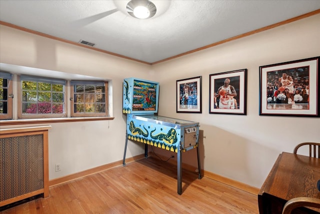 game room with ornamental molding, a textured ceiling, radiator, and light wood-type flooring