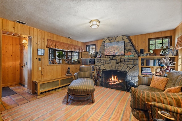 living room with wooden walls, a stone fireplace, a textured ceiling, and tile patterned flooring