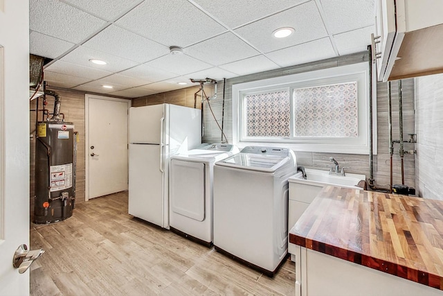 clothes washing area with water heater, cabinets, washing machine and clothes dryer, light hardwood / wood-style floors, and wood walls