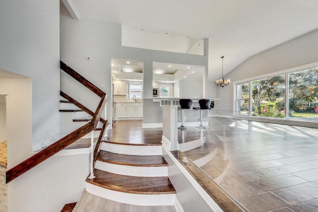 stairs featuring high vaulted ceiling, hardwood / wood-style floors, a chandelier, and sink