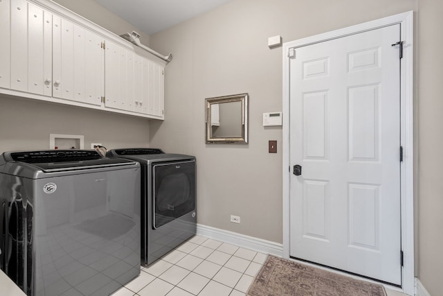 clothes washing area with washing machine and clothes dryer, cabinets, and light tile patterned floors