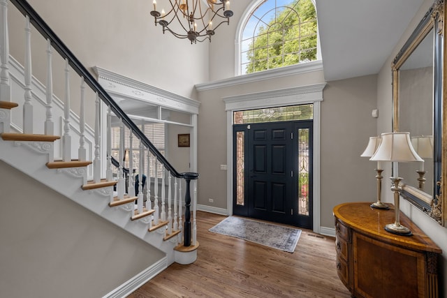 entryway with a towering ceiling, a chandelier, and wood-type flooring