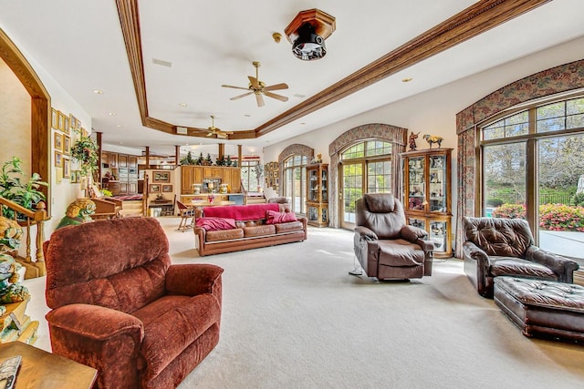 living room featuring a raised ceiling, ornamental molding, carpet, and ceiling fan