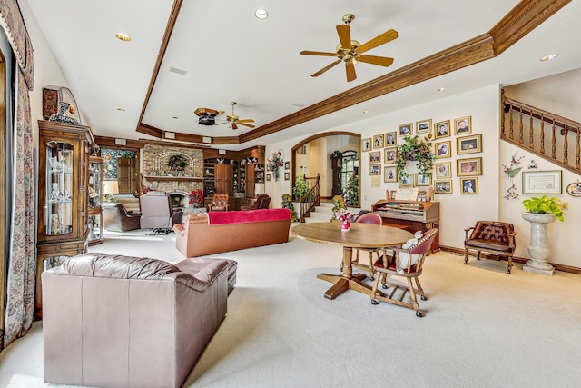 living room with a large fireplace, ornamental molding, light colored carpet, ceiling fan, and a tray ceiling