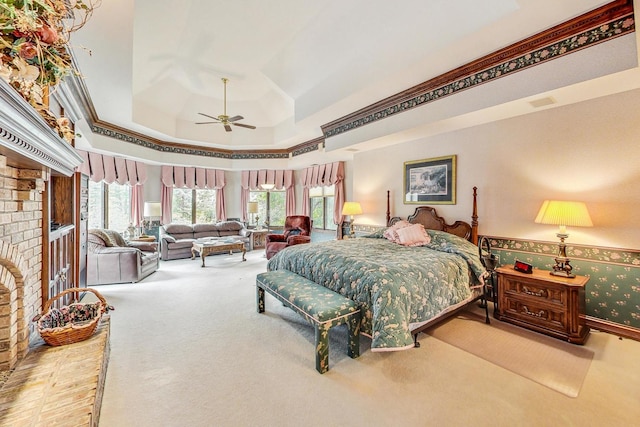 bedroom with crown molding, a brick fireplace, a tray ceiling, carpet floors, and ceiling fan