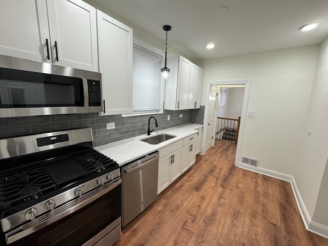 kitchen with dark hardwood / wood-style floors, white cabinets, sink, hanging light fixtures, and appliances with stainless steel finishes