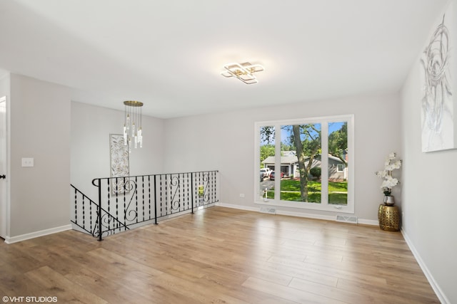 empty room with light hardwood / wood-style flooring and a chandelier