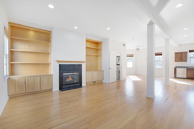 unfurnished living room with a fireplace, built in shelves, light wood-type flooring, and ceiling fan