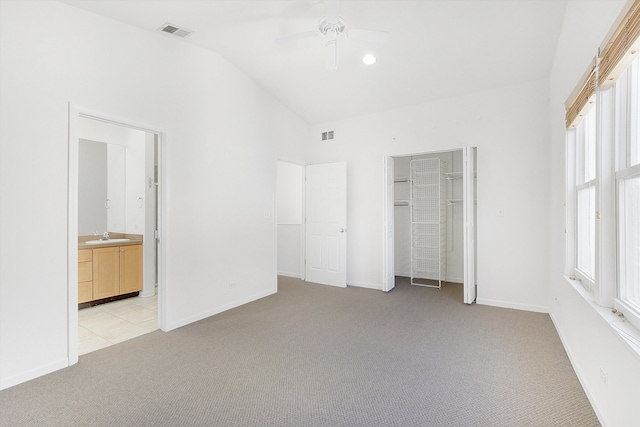 unfurnished bedroom featuring ceiling fan, light colored carpet, ensuite bath, and vaulted ceiling