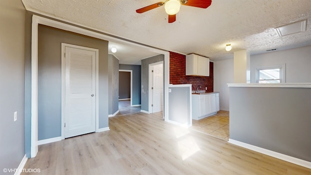 unfurnished living room with light hardwood / wood-style floors, a textured ceiling, sink, and ceiling fan