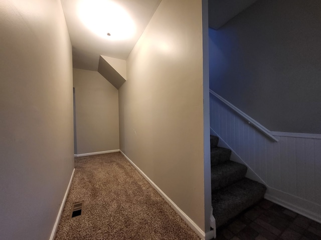 staircase with carpet flooring, wooden walls, and vaulted ceiling