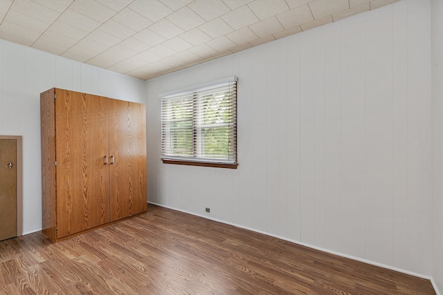 unfurnished bedroom featuring wooden walls, a closet, and hardwood / wood-style floors