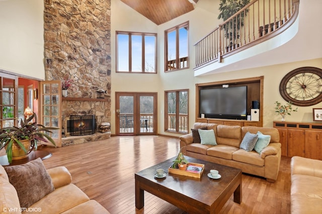 living room with a stone fireplace, a towering ceiling, wooden ceiling, and light wood-type flooring