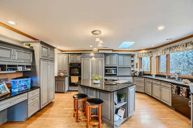 kitchen featuring gray cabinetry, a center island, dark stone counters, sink, and a skylight